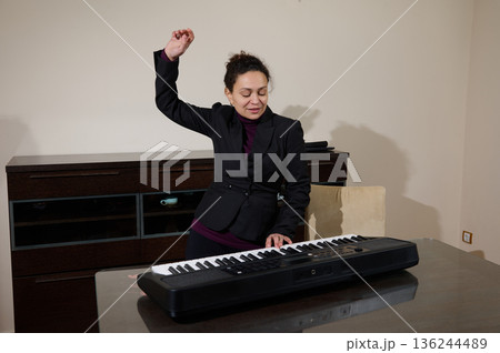 Professional Woman In Suit Plays Keyboard At Office Desk, Expressing Joy And Focus Professional Woman In Suit Plays Keyboard At Office Desk, Expressing Joy And Focus 136244489