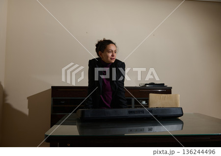 Professional Woman in Office Leaning Over Desk with Keyboard in Modern Studio Setting Professional Woman in Office Leaning Over Desk with Keyboard in Modern Studio Setting 136244496