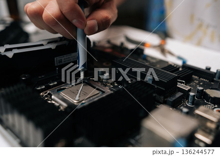 Technician hand applying thermal paste to CPU of computer motherboard, demonstrating process of computer maintenance and repair in dark workshop. Concept of computer hardware, repairing 136244577