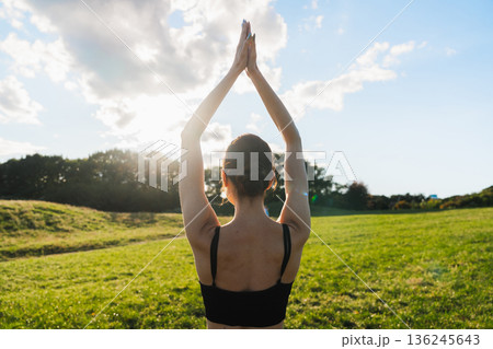 Practicing mindful yoga in a serene green field under the bright sun 136245643