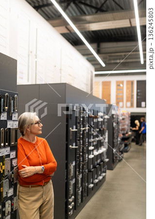 Woman shopping for home improvement items in a modern hardware store with a wide selection of tools 136245803