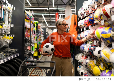 Woman shopping for sports equipment and holding a soccer ball in a sporting goods store during the Woman shopping for sports equipment and holding a soccer ball in a sporting goods store during the 136245874