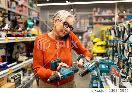 Woman shopping for tools in a hardware store while talking on the phone in the afternoon Woman shopping for tools in a hardware store while talking on the phone in the afternoon 136245942