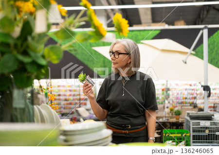 Senior woman shopping for plants in a garden center surrounded by vibrant flowers and gardening 136246065