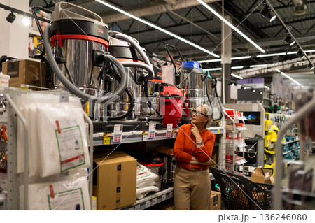 Woman shopping for cleaning equipment in a hardware store while considering options for a new vacuum 136246080