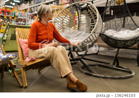 Woman explores unique hanging chairs in a home decor store during a relaxed shopping experience 136246103