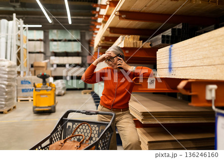Woman in orange sweater talks on phone while sitting on cart in a lumber store during the day 136246160