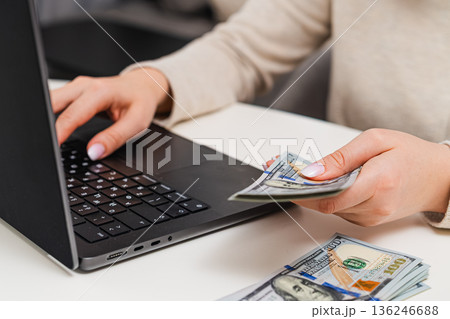 Female managing finances, counting cash and recording expenses on laptop. Savings, income tracking, and financial literacy. Female managing finances, counting cash and recording expenses on laptop. Savings, income tracking, and financial literacy. 136246688