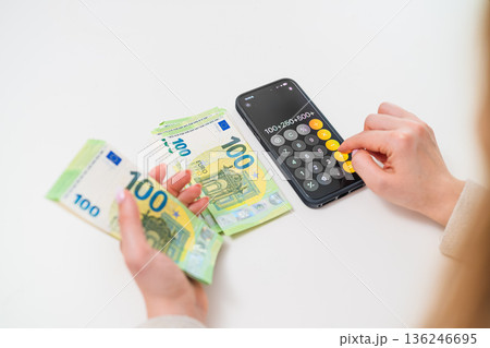Top view of woman counting euro banknotes and using smartphone calculator. Concept of savings, budgeting, and european economy. Top view of woman counting euro banknotes and using smartphone calculator. Concept of savings, budgeting, and european economy. 136246695