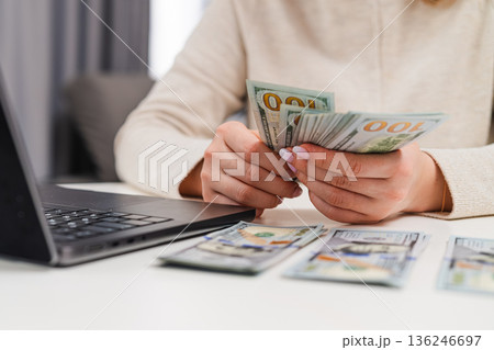 Woman counting us dollar banknotes while entering financial data on computer. Concept of accounting and personal finance management. Woman counting us dollar banknotes while entering financial data on computer. Concept of accounting and personal finance management. 136246697
