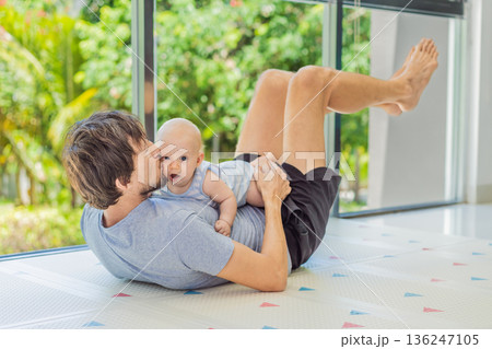 Father exercising with his small baby at home, active parenting and healthy lifestyle. Strong family bond, early physical development, modern fatherhood, fitness with children concept. Father exercising with his small baby at home, active parenting and healthy lifestyle. Strong family bond, early physical development, modern fatherhood, fitness with children concept. 136247105