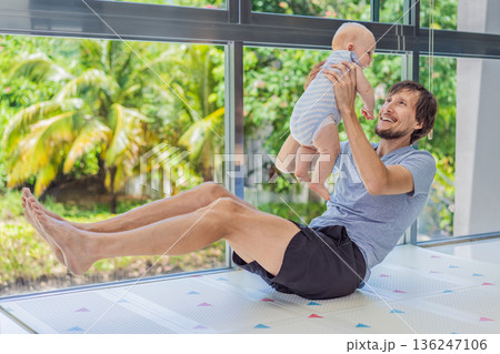 Father exercising with his small baby at home, active parenting and healthy lifestyle. Strong family bond, early physical development, modern fatherhood, fitness with children concept. Father exercising with his small baby at home, active parenting and healthy lifestyle. Strong family bond, early physical development, modern fatherhood, fitness with children concept. 136247106