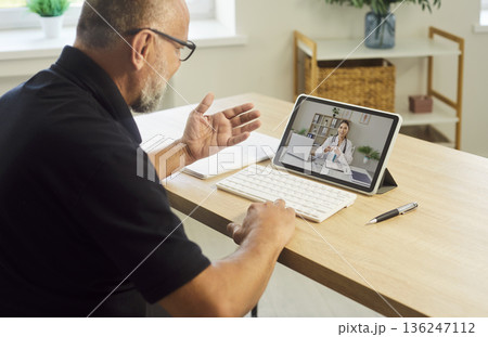 Senior man consulting doctor via telemedicine on tablet with keyboard at home desk Senior man consulting doctor via telemedicine on tablet with keyboard at home desk 136247112