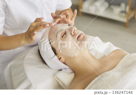 Beautician or cosmetologist applying moisturizing sheet mask on young woman face 136247148