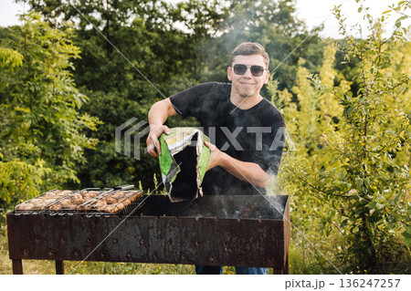 Man pouring charcoal into grill, lighting fire for mushroom barbecue outdoors Man pouring charcoal into grill, lighting fire for mushroom barbecue outdoors 136247257
