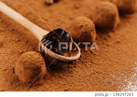Bitten chocolate truffle on wooden spoon over cocoa powder background 136247263