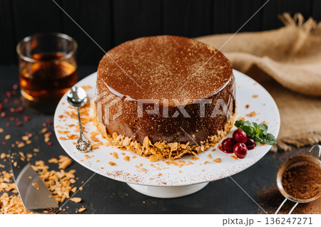 Close up glossy chocolate cake with crumbs and cocoa on white plate, dark background Close up glossy chocolate cake with crumbs and cocoa on white plate, dark background 136247271