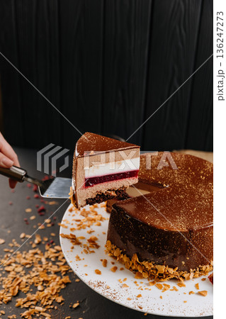 Layered chocolate mousse cake slice with raspberry jelly on spatula, dark background 136247273