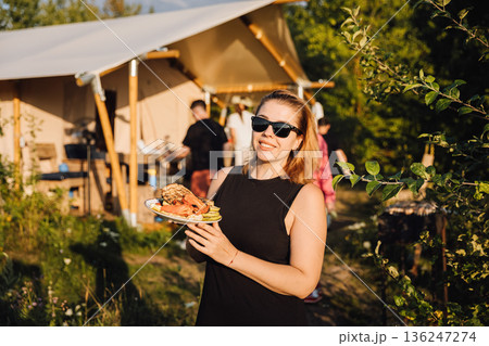 Woman holding plate of grilled vegetables at outdoor barbecue party near camping tent Woman holding plate of grilled vegetables at outdoor barbecue party near camping tent 136247274