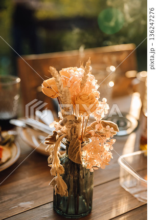 Peach flower bouquet in vase on rustic table, golden hour outdoor dinner 136247276