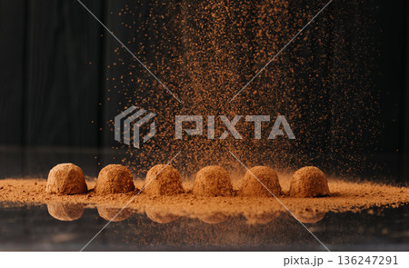 Cocoa powder falling over chocolate truffles with reflection on black background 136247291