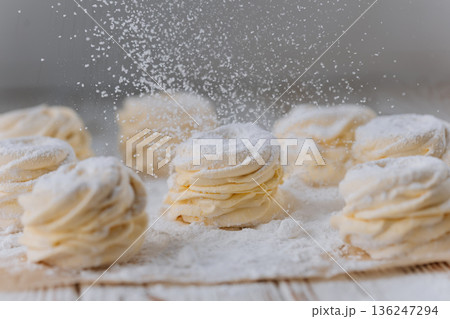 Powdered sugar falling on vanilla zephyr rosettes on parchment, rustic background 136247294