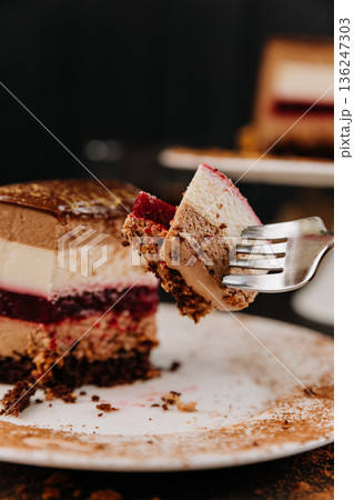 Fork with bite of layered chocolate mousse cake and berry jelly closeup 136247303