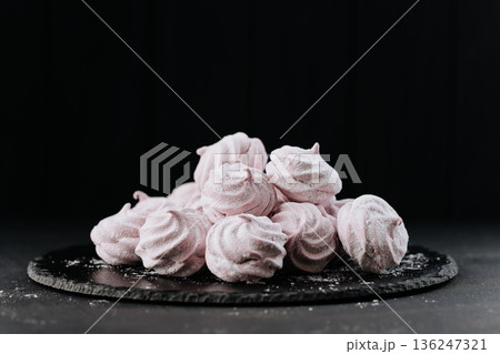 Pink meringue cookies on slate plate, dark background, powdered sugar 136247321
