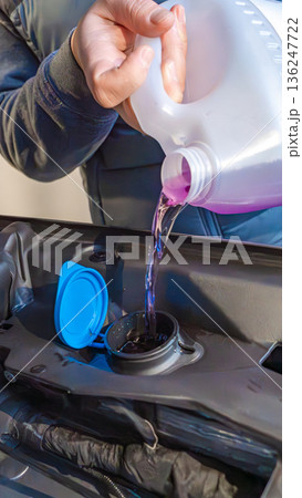 Person pouring purple liquid into a car's reservoir cap, showcasing automotive maintenance in a close-up view of the engine compartment Person pouring purple liquid into a car's reservoir cap, showcasing automotive maintenance in a close-up view of the engine compartment 136247722
