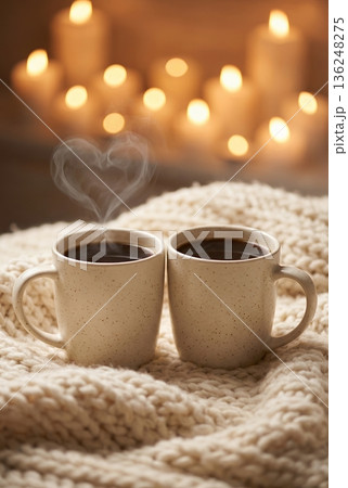 Two coffee mugs with heart-shaped steam on cozy blanket with candles 136248275