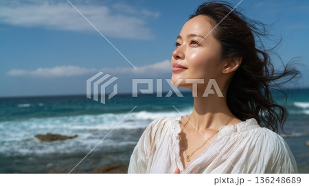 Woman with windblown hair smiling by ocean Woman with windblown hair smiling by ocean 136248689