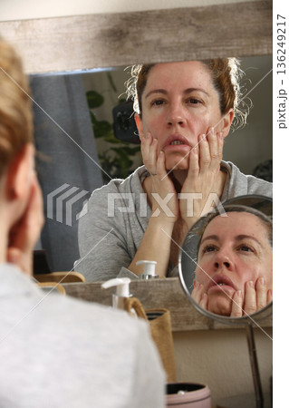 Mature Woman Practicing Face Yoga in Front of Mirror 136249217