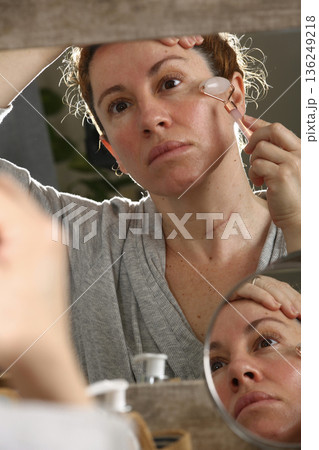 Mature Woman Practicing Face Yoga in Front of Mirror 136249218