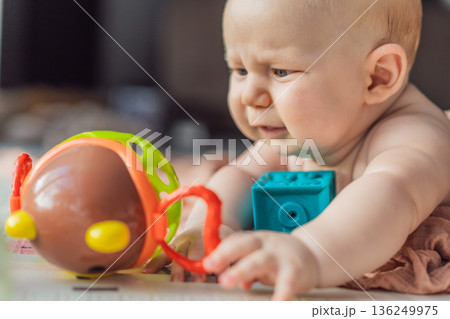 Little baby playing with toys on a soft baby play mat at home. Early childhood development, sensory play, learning through play, curiosity, and happy infant activity concept for modern parenting. 136249975
