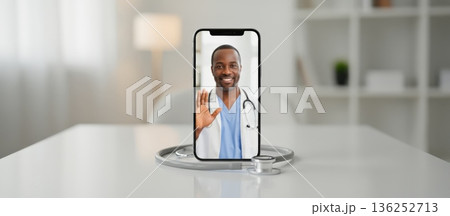 African american male doctor talking to patient during app video call on smartphone with stethoscope on white table, representing modern telehealth and online medical consultation 136252713