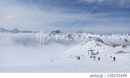 Ski slope with skiers above clouds Ski slope with skiers above clouds 136253349
