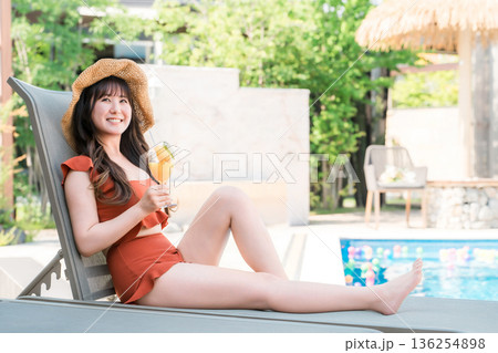 プールサイドのリクライニングチェアに座りトロピカルジュースを飲む水着姿の若いアジア人女性 プールサイドのリクライニングチェアに座りトロピカルジュースを飲む水着姿の若いアジア人女性 136254898