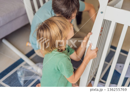 Father and older brother assembling a baby crib at home, preparing for a newborn arrival. Warm family moment full of care and anticipation. Parenthood, sibling bond and home preparation concept Father and older brother assembling a baby crib at home, preparing for a newborn arrival. Warm family moment full of care and anticipation. Parenthood, sibling bond and home preparation concept 136255769