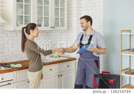 Repairman in uniform shaking hands with woman after successful repair standing in kitchen Repairman in uniform shaking hands with woman after successful repair standing in kitchen 136258784