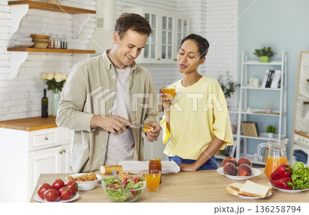 Couple preparing toast with jam and drinking juice together in bright kitchen 136258794