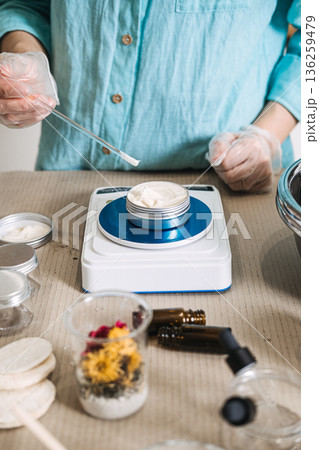 Person in gloves uses glass rod to apply cream into metal tin on digital scale. Botanical ingredients aesthetic, raw beauty materials, herbal mixology, natural skincare components. Person in gloves uses glass rod to apply cream into metal tin on digital scale. Botanical ingredients aesthetic, raw beauty materials, herbal mixology, natural skincare components. 136259479