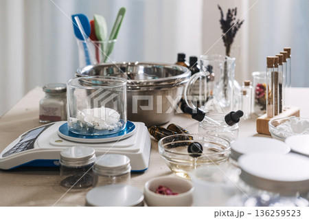 Glass beaker with solid oil sits on digital scale surrounded by laboratory equipment and ingredients. Custom oil blending, bespoke facial oils, personalized skincare routine, targeted beauty oils. 136259523