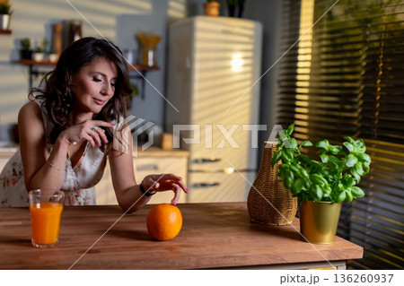 Caucasian woman reaching orange on table with thoughtful gesture, closeup of hand and fruit against warm kitchen background, moment of mindful eating and intentional selection Caucasian woman reaching orange on table with thoughtful gesture, closeup of hand and fruit against warm kitchen background, moment of mindful eating and intentional selection 136260937