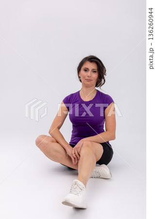 Seated woman on studio floor cooling one knee bent, relaxed expression, posttraining stretch, white sneakers, black shorts, recovery routine, mindful breathing, balanced wellness Seated woman on studio floor cooling one knee bent, relaxed expression, posttraining stretch, white sneakers, black shorts, recovery routine, mindful breathing, balanced wellness 136260944