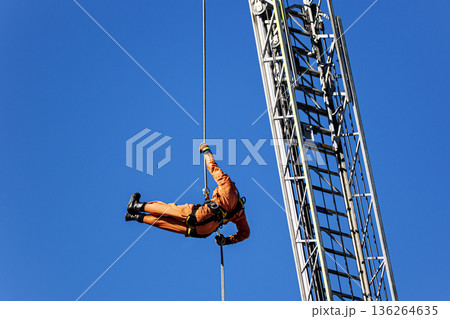 出初式ではしご付消防車の高く伸ばしたはしごからロープによる降下訓練を行うレンジャー消防隊員 136264635