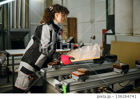 Woman works on wood in a carpentry workshop with tools and machinery in the background Woman works on wood in a carpentry workshop with tools and machinery in the background 136264741