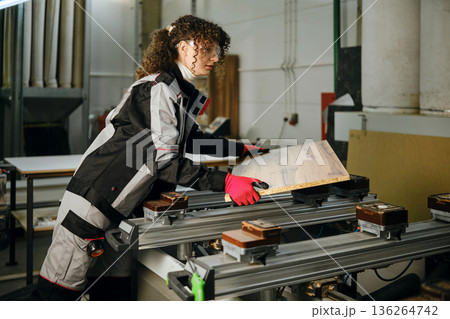 Woman is laying a wooden panel on a milling machine Woman is laying a wooden panel on a milling machine 136264742