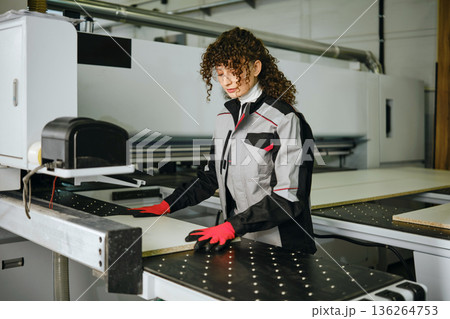Woman works on CNC machine in factory during day while wearing gloves and safety gear Woman works on CNC machine in factory during day while wearing gloves and safety gear 136264753