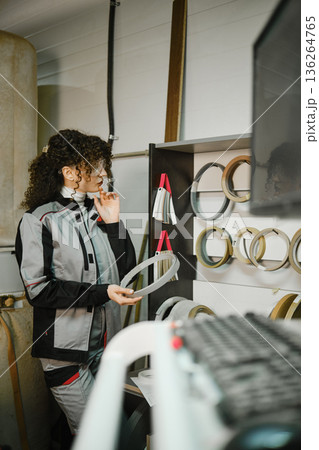 Woman examines metal rings in workshop while wearing work clothing and safety glasses Woman examines metal rings in workshop while wearing work clothing and safety glasses 136264765