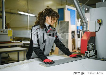 Woman operates woodworking machine in workshop during daytime 136264767